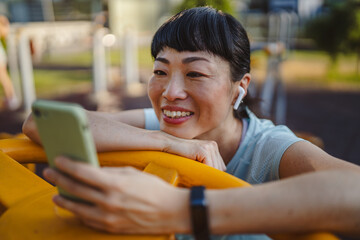 Japanese woman in a sportswear stand in park and use mobile phone