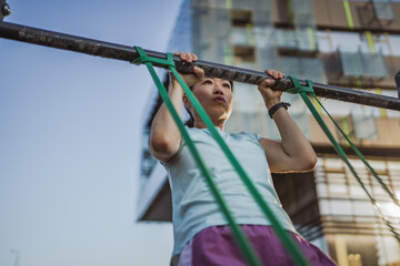japanese woman doing pulls up on bar at outdoor open gym in park