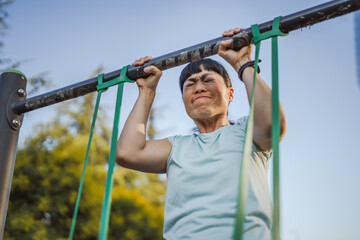 japanese woman doing pulls up on bar at outdoor open gym in park