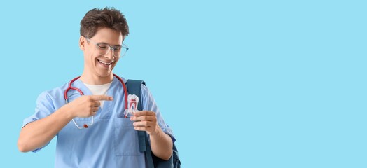 Male medical student with tooth model on blue background with space for text