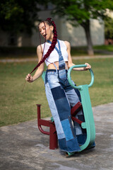 Playful young woman with long braids on park exercise equipment