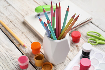Holder with different color pencils and paints on light wooden background