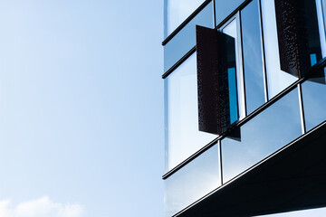 Contemporary architecture detail showing reflective glass facade with open windows. Image highlights urban design and modern construction elements.