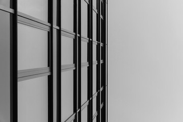 Black and white photo of a modern glass building facade with strong geometric lines. The image emphasizes architectural structure and urban design.