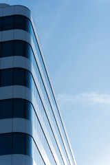 Contemporary office building with curved glass and metal facade, photographed against a clear blue sky. The image highlights modern architecture and urban business environments.