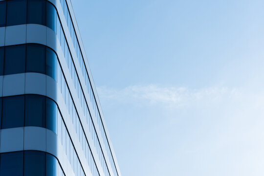 Photo shows a contemporary office building with curved glass windows and white panels. The structure is set against a clear blue sky, emphasizing modern architecture and urban business environments.