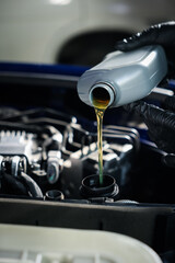 Worker pouring motor oil from bottle into car engine, closeup