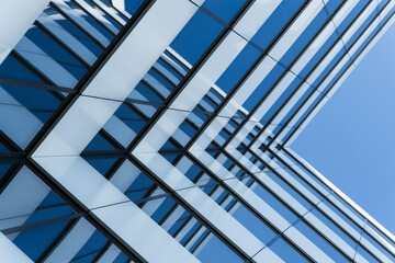 Close-up view of a contemporary glass office building with geometric lines reflecting a clear blue sky. The image emphasizes modern architecture and urban design for business or construction concepts.