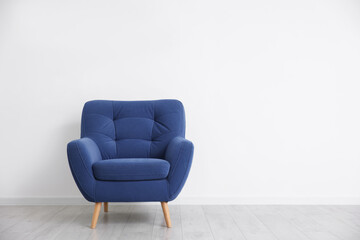 Comfortable blue armchair near white wall indoors, space for text