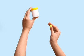 Female hands holding bottle of pills on blue background