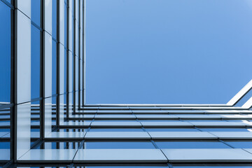 Photo shows the upward perspective of a modern glass office building with reflective windows. The...