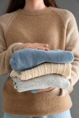 Woman holding stack of different stylish sweaters on grey background, closeup