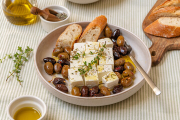Feta cheese served on a plate with assorted olives, garnished with herbs and lemon slices and...