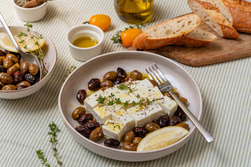 Feta cheese served on a plate with assorted olives, garnished with herbs and lemon slices and crusty bread, traditional Greek or Italian food, Mediterranean diet