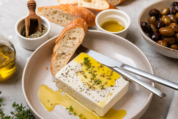 Feta cheese served on a plate with assorted olives, garnished with herbs and lemon slices and crusty bread, traditional Greek or Italian food, Mediterranean diet