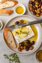 Feta cheese served on a plate with assorted olives, garnished with herbs and lemon slices and crusty bread, traditional Greek or Italian food, Mediterranean diet