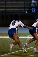 A female flag football player charges forward with determination during a night game. Capturing speed, focus, and competitive spirit under stadium lights on the turf.