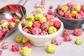 Bowls and metal scoop with sweet colorful popcorn on white background