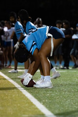 Female flag football center prepares to snap under the stadium lights. Focused stance, ready hands, and team alignment showcase precision and preparation in youth sports.