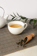 Bamboo mat with teapot, cup of tea and leaves on grunge table against white background