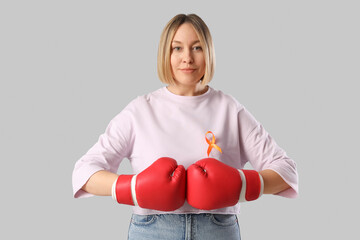 Happy mature woman in boxing gloves with ribbon on grey background. Multiple Sclerosis Awareness...