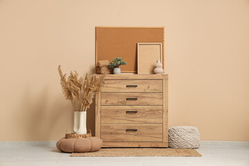Chest of drawers, pampas grass, pouf and frames near beige wall