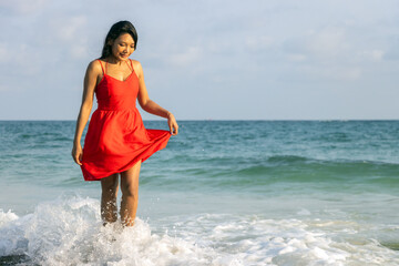 A woman in a red dress walk in waves at sea shore