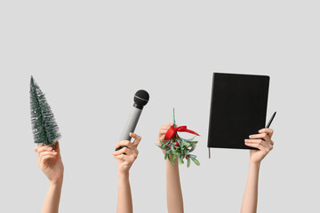 Journalist's female hands with Christmas decorations, notebook and microphone on grey background