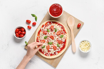Female hand with raw pizza and ingredients on white grunge background