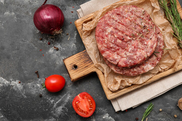 Cutting board with raw meat cutlets on grey grunge background
