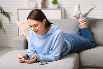 Young diabetic woman taking blood sample with lancet pen at home