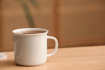 Mug of hot tea on wooden table on blurred background. Closeup