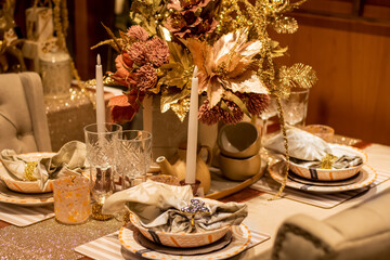 Elegant Christmas dinner table set decoration in gold with glasses, candles and plates