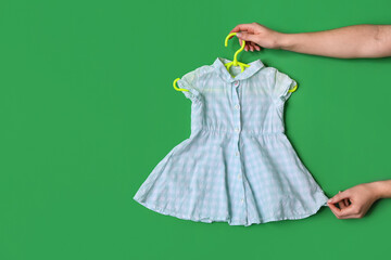 Female hands with stylish baby dress on green background