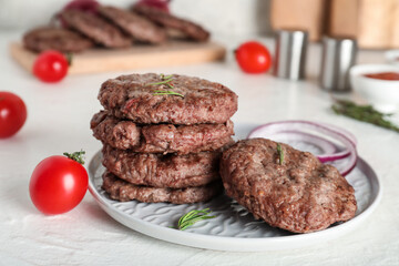 Plate with tasty meat cutlets, tomato, onion rings and rosemary on white background
