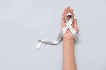 Woman holding awareness ribbon on grey background. Brain cancer concept