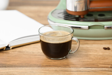 Glass cup of hot espresso with modern coffee machine and book on wooden background