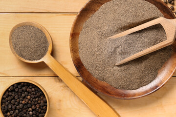 Bowl and spoon of black pepper powder with peppercorns on wooden background