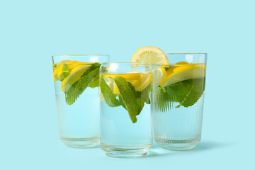 Glasses of water with lemon slices and mint leaves on blue background