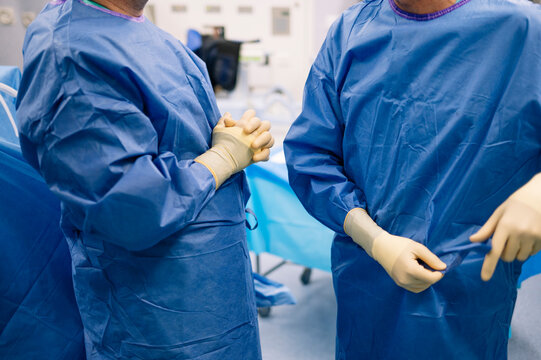 Two surgeons dressed in blue surgical gowns prepare for procedure inside operating room - Powered by Adobe