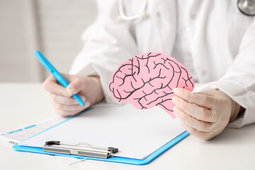 Female doctor with paper brain writing on clipboard at table in clinic, closeup. Brain cancer...