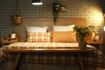 Big comfortable bed and bedside tables near grey brick wall in interior of bedroom at night