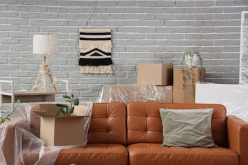 Brown sofa with film and cardboard box in living room on moving day
