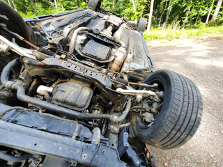 An overturned vehicle rests on its roof amidst trees gravel, indicating recent accident in quiet location.