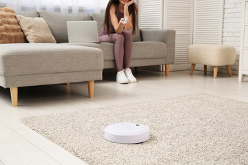 Robot vacuum cleaner on carpet against sporty woman at home, closeup