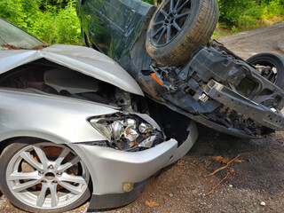 Serious car accident on quiet road involves damaged silver sedan an overturned black car.