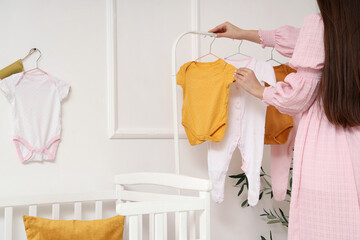 Young woman near rack with baby bodysuits in nursery, back view