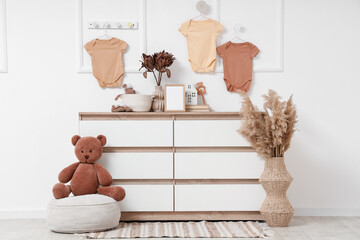 Interior of nursery with commode, pouf and hanging baby bodysuits