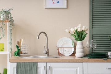 Interior of festive kitchen with utensils, flowers and Easter decorations on counter near beige wall