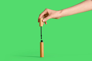 Female hand with black mascara on green background